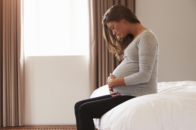 Pregnant woman holding stomach while on bed.